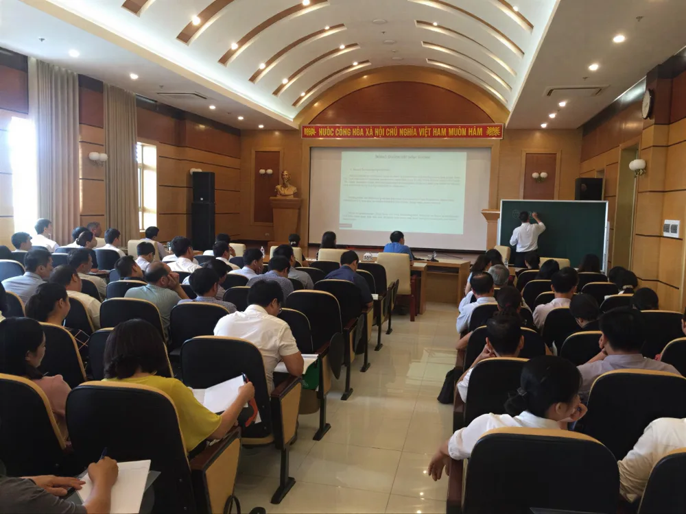 Hội trường lớp đào tạo nghiệp vụ đông học viên, giảng viên trình bày bên màn hình chiếu và bảng viết phía trước.