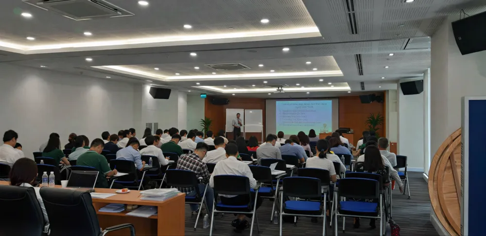 Lớp học nghiệp vụ trong không gian hiện đại với tường ốp gỗ, học viên ngồi theo dãy bàn và màn hình trình chiếu.